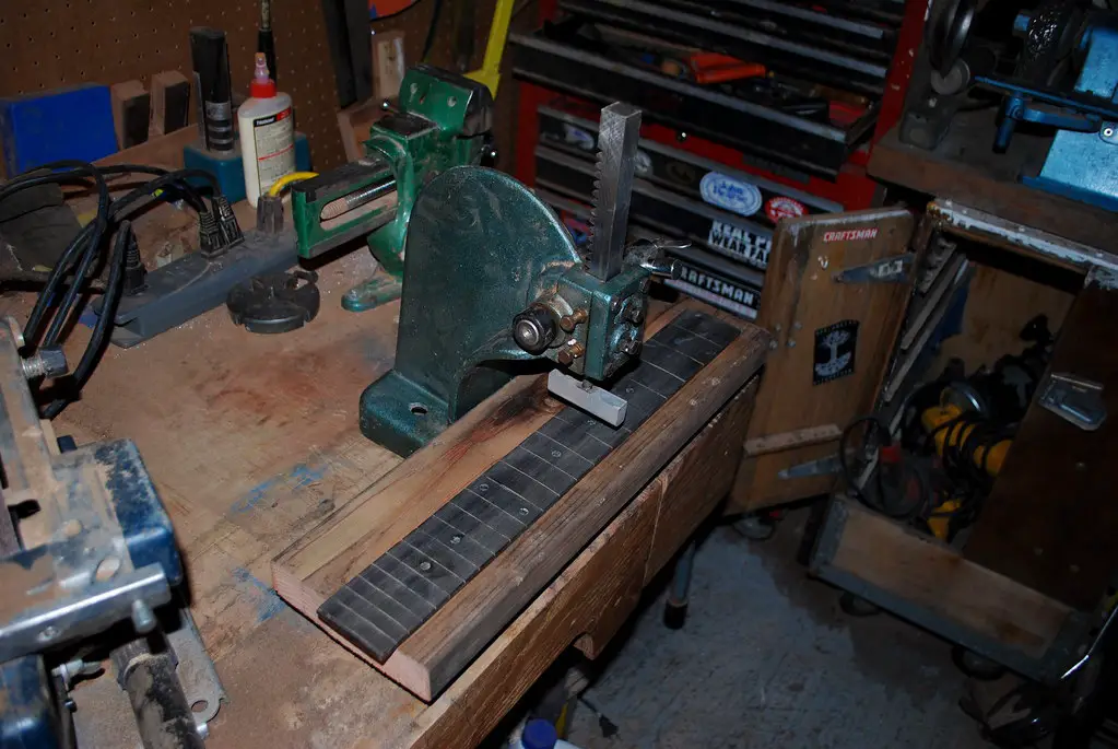 A small arbor press being used to press frets into the neck of a guitar.