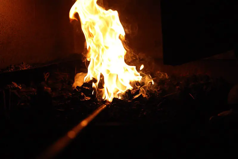 A piece of round stock sits in the hot bed of a forge.