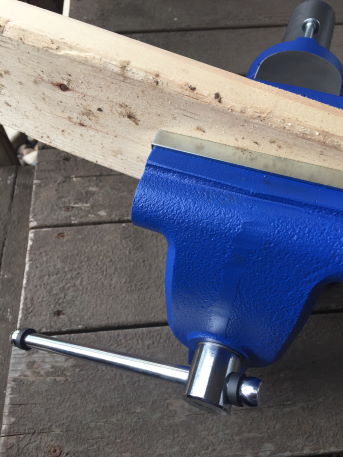 a cedar board clamped in a metal working vise