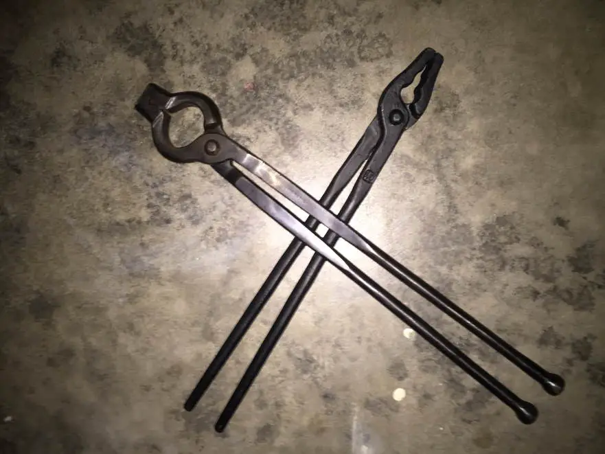 Two blacksmithings tongs crossed on a concrete garage floor