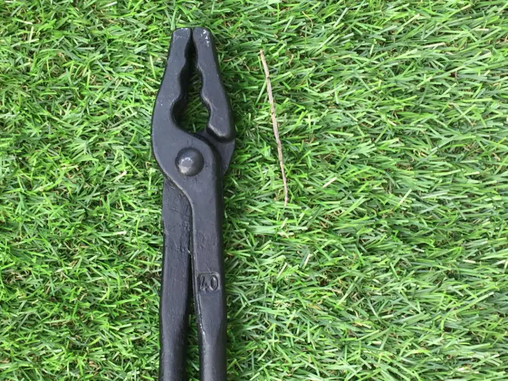 A pair of wolf jaw tongs lying down on faux turf.