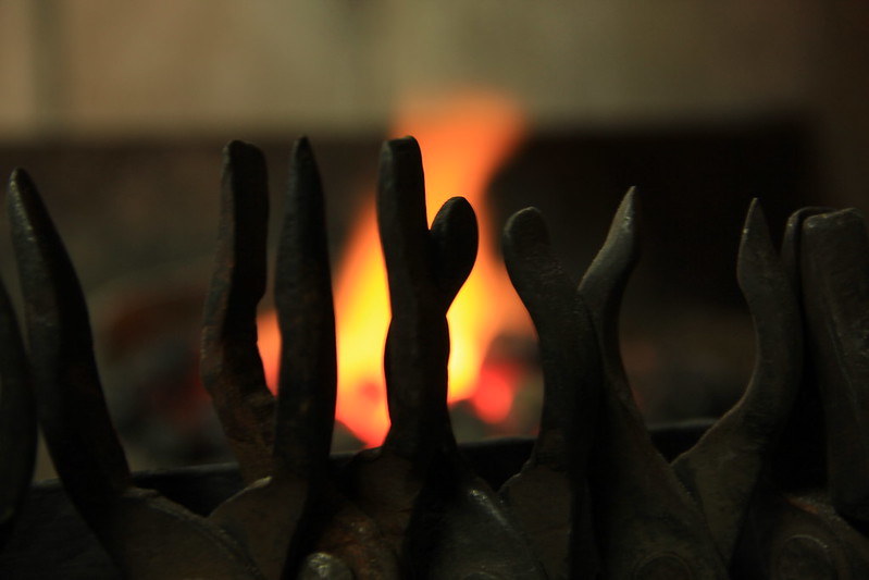 Blacksmithing tongs on a rack with a forge fire in the background